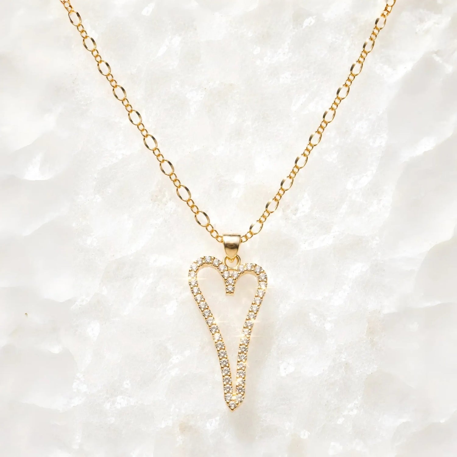 Cara gold Heart A necklace with pavé crystal pendant on a delicate gold chain displayed on a white crystal quartz background.