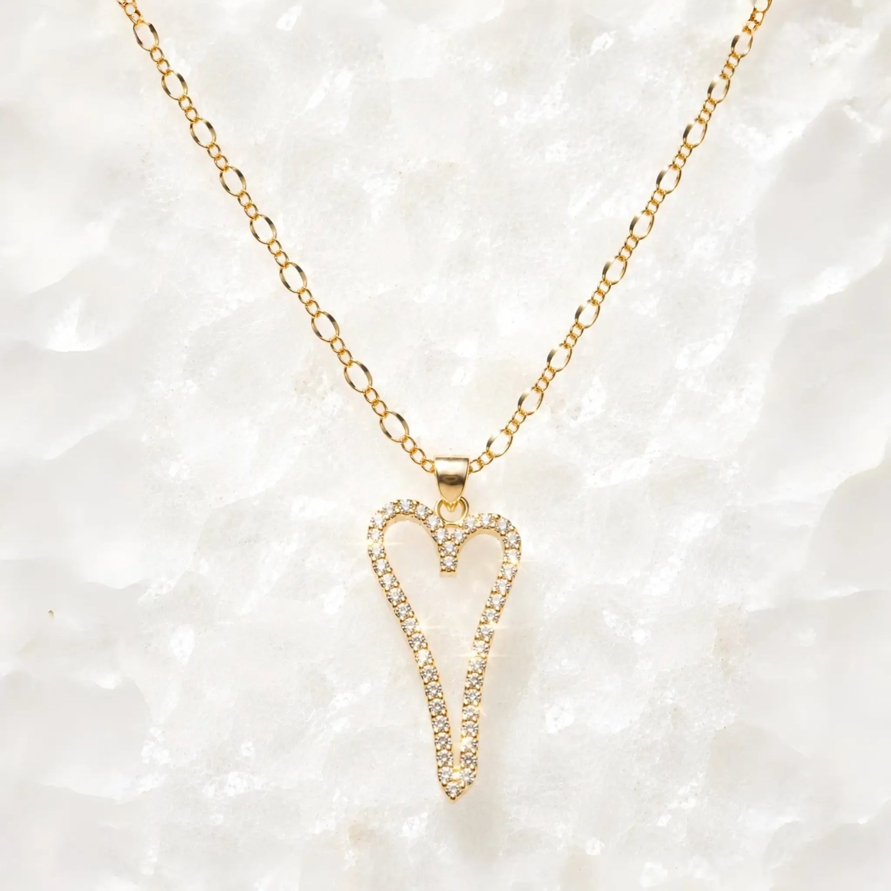 Cara gold Heart A necklace with pavé crystal pendant on a delicate gold chain displayed on a white crystal quartz background.