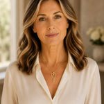 Woman wearing the Cara gold Heart A necklace with an ivory silk blouse in a refined luxury interior.
