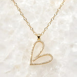 Cara gold Heart B necklace with pavé crystal pendant on a delicate gold chain displayed on a white crystal quartz background.