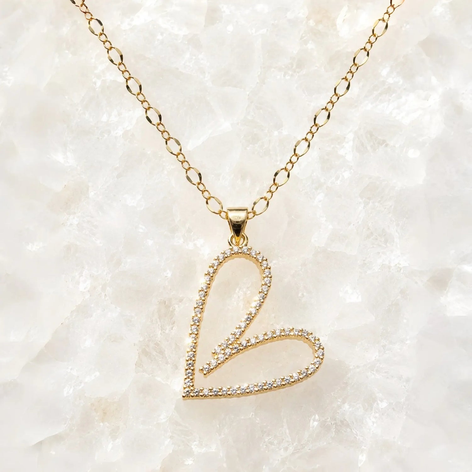 Cara gold Heart B necklace with pavé crystal pendant on a delicate gold chain displayed on a white crystal quartz background.