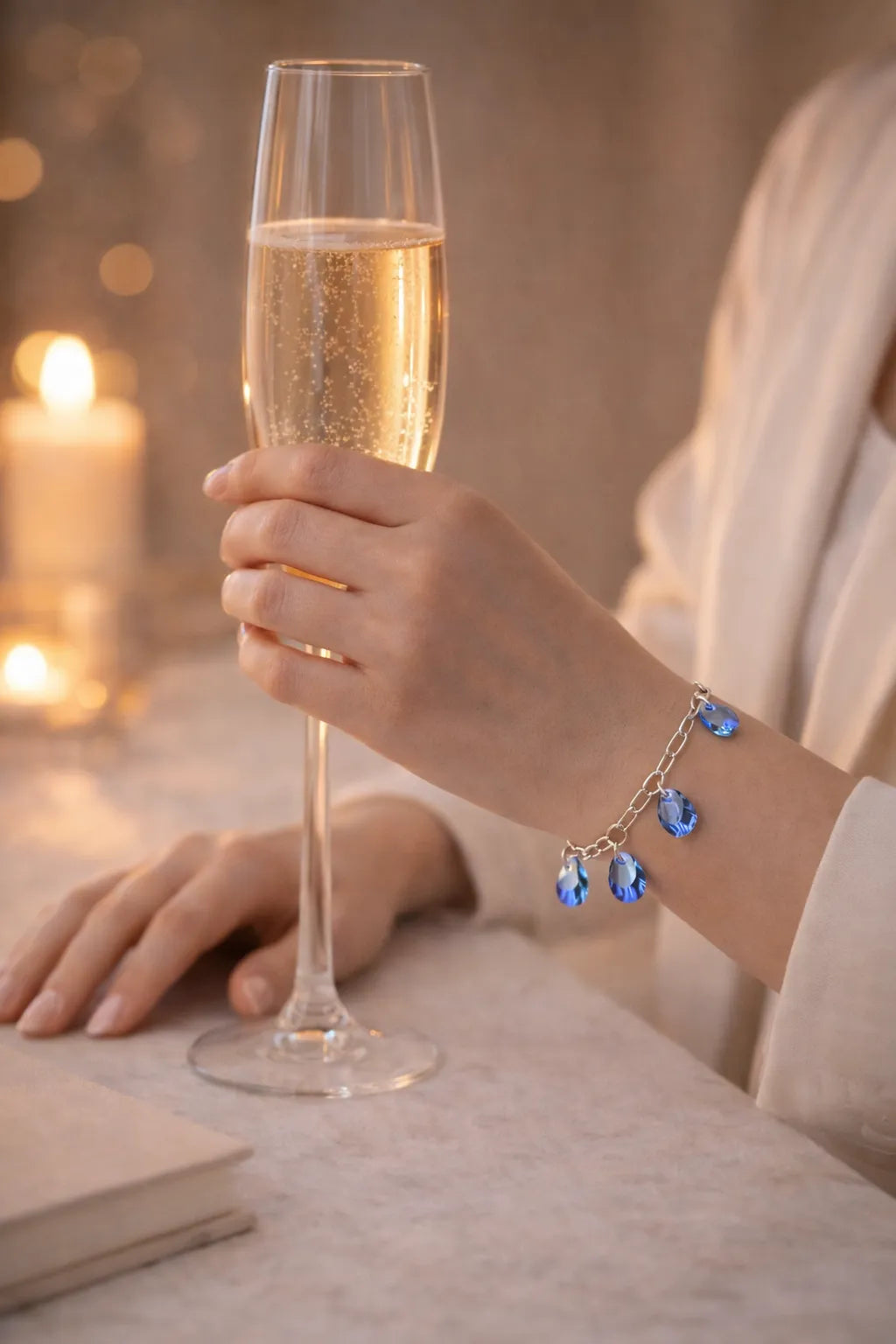 Blue crystal charm bracelet worn while holding champagne glass in warm evening light