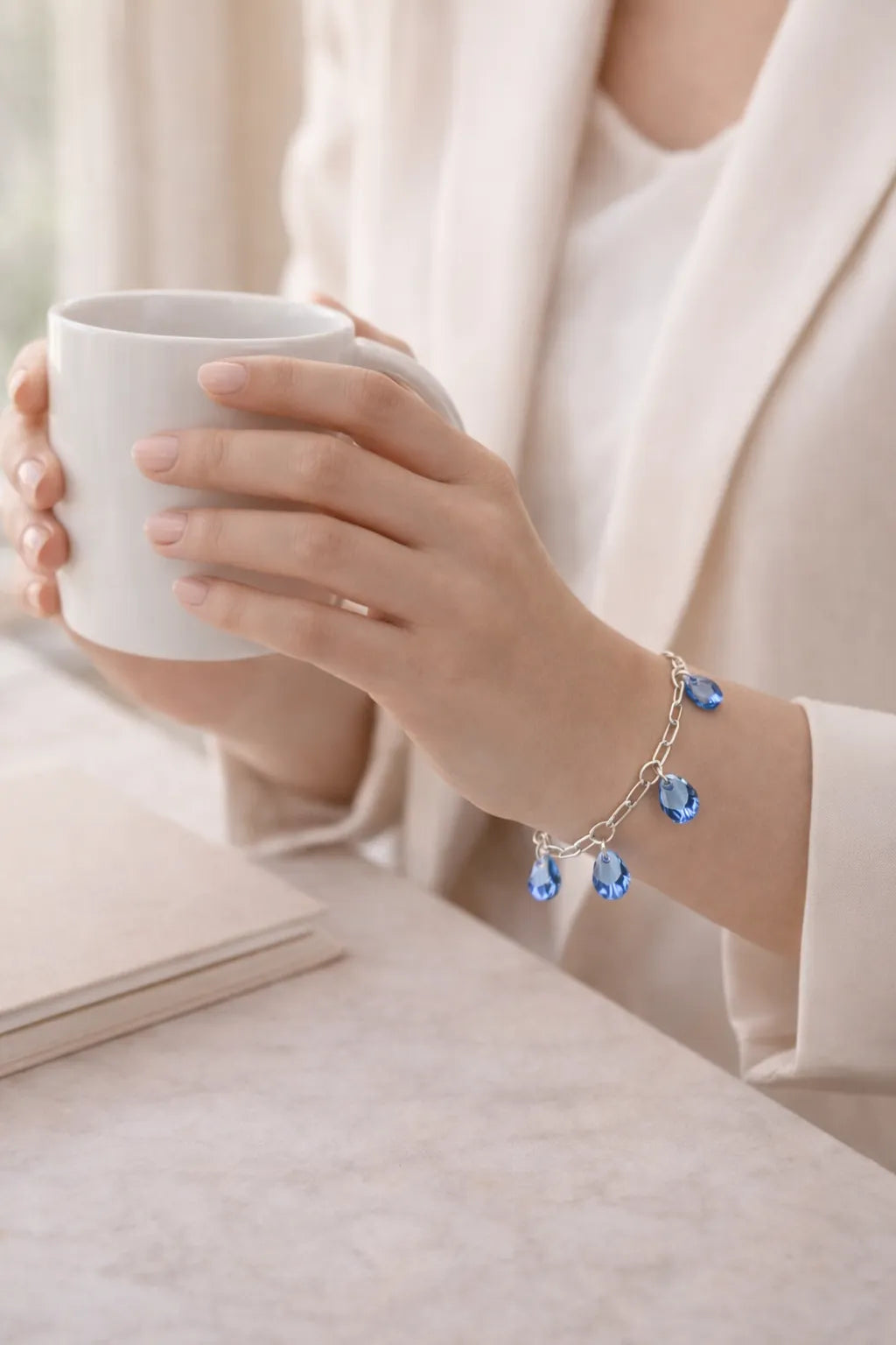 Blue crystal charm bracelet worn while holding coffee cup in soft morning light