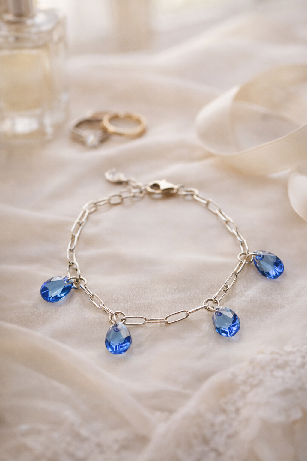 Blue crystal charm bracelet by Carabella by Cheryl styled on ivory silk with bridal rings and perfume