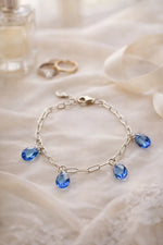 Blue crystal charm bracelet by Carabella by Cheryl styled on ivory silk with bridal rings and perfume