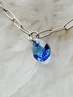 Close-up of sterling silver charm bracelet with sapphire blue crystal drop by Carabella by Cheryl
