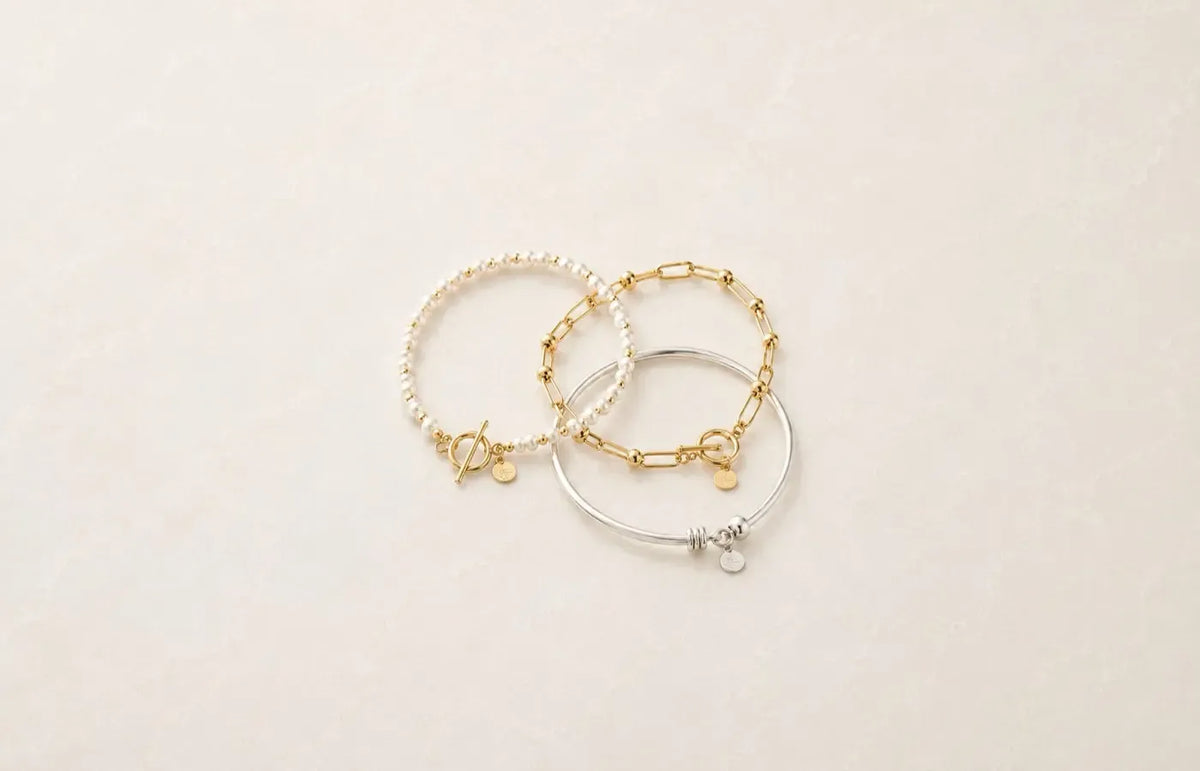 Pearl, gold and silver bracelets styled together on a soft neutral background.