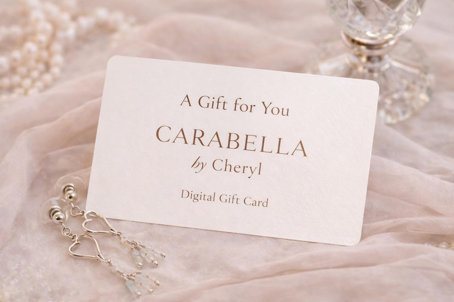 Carabella by Cheryl digital gift card styled with sterling silver heart earrings, soft blush fabric, pearls, and crystal accents in an elegant luxury setting.