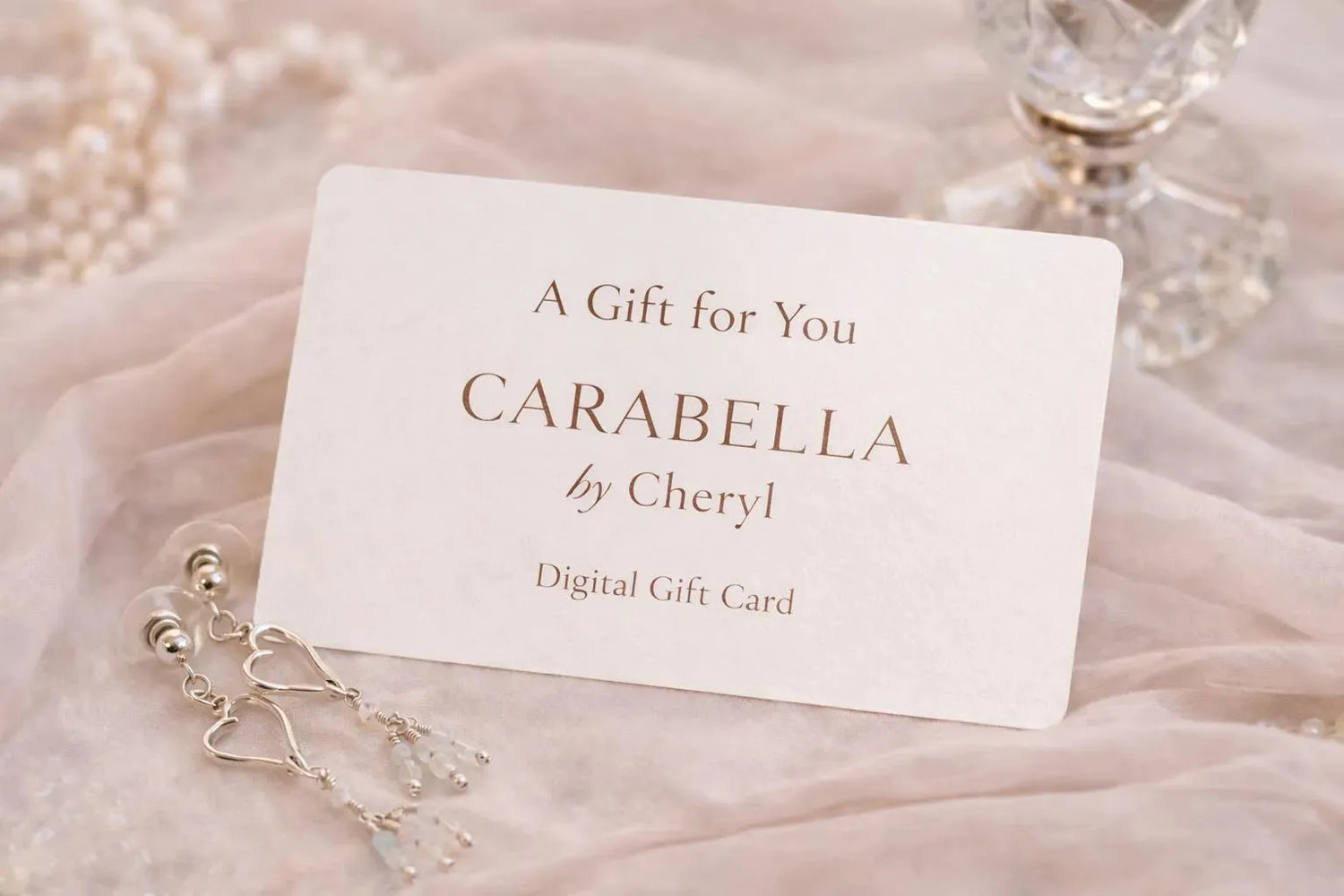 Carabella by Cheryl digital gift card styled with sterling silver heart earrings, soft blush fabric, pearls, and crystal accents in an elegant luxury setting.