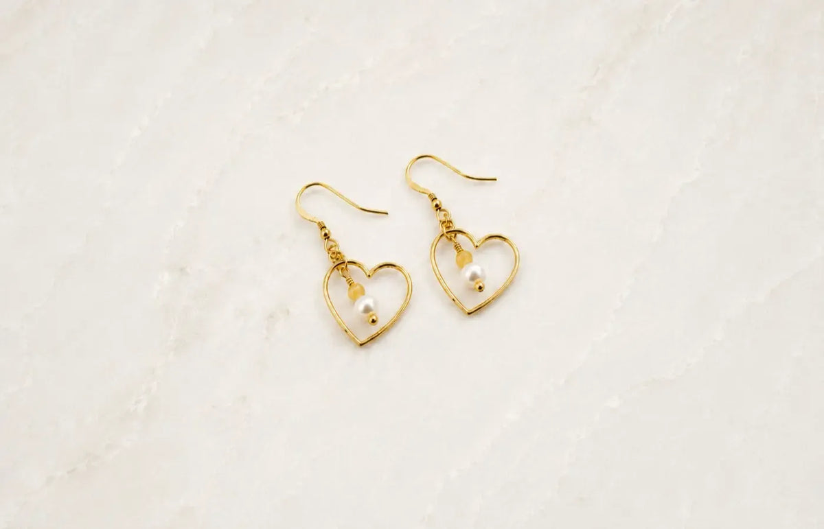 Gold heart drop earrings with pearl and gemstone details on ivory stone