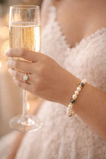 Bride holding a champagne flute during a wedding toast while wearing a Carabella pearl bridal bracelet.