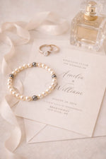 Carabella pearl bridal bracelet styled beside a wedding invitation, silk ribbon, rings, and perfume bottle.