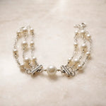 Cream European crystal pearl bracelet with sterling silver toggle accents and central focal pearl, styled on a soft alabaster surface in a refined luxury editorial setting.
