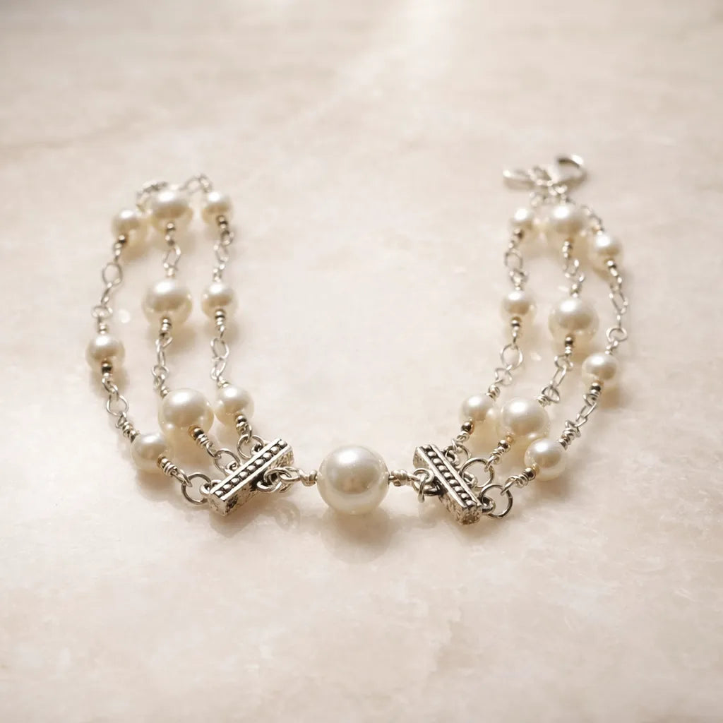 Cream European crystal pearl bracelet with sterling silver toggle accents and central focal pearl, styled on a soft alabaster surface in a refined luxury editorial setting.