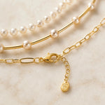 Macro detail of the Cassia necklace showing the polished gold lobster clasp, extender chain, signature charm, paperclip chain, gold tube strand and Swarovski® Crystal Pearls.