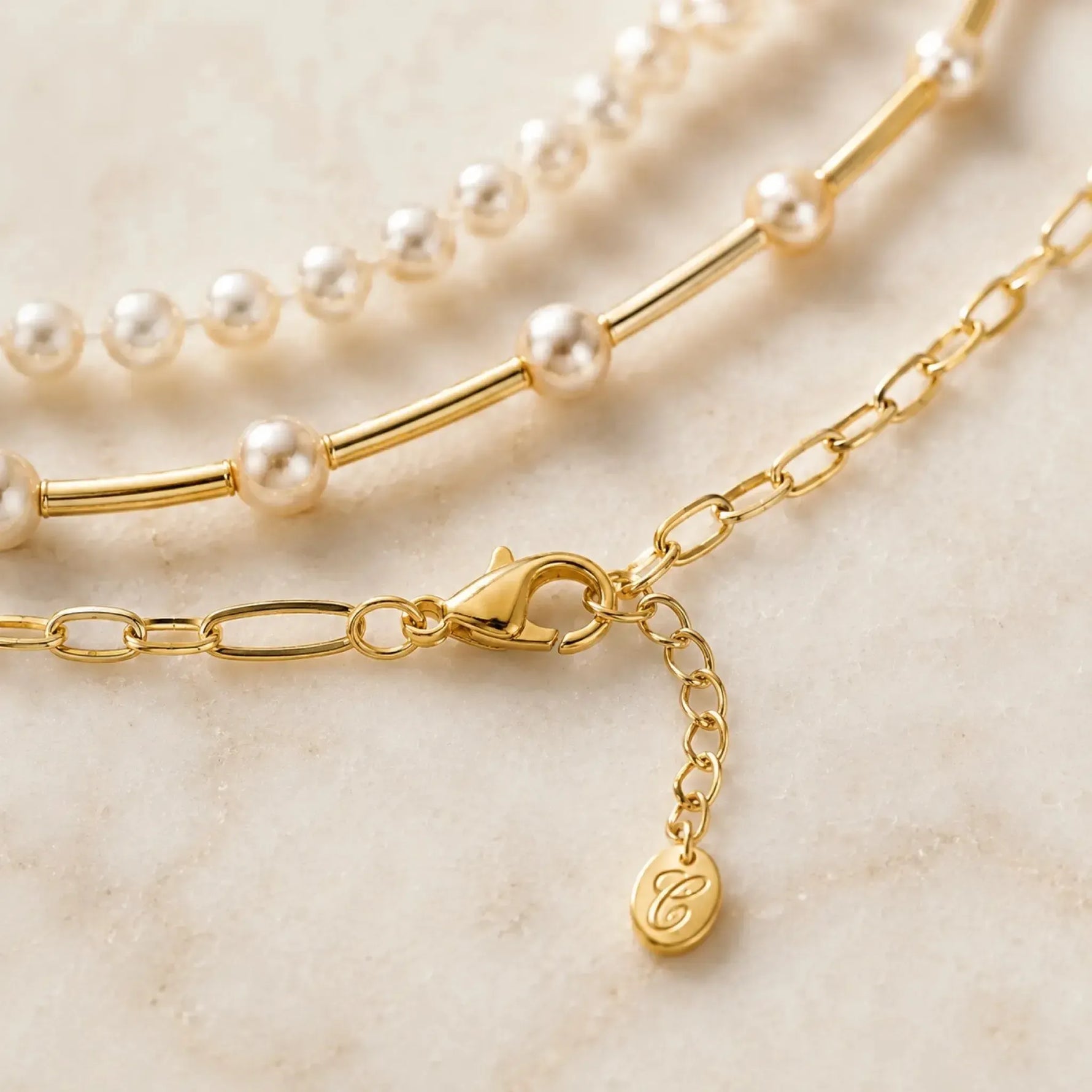 Macro detail of the Cassia necklace showing the polished gold lobster clasp, extender chain, signature charm, paperclip chain, gold tube strand and Swarovski® Crystal Pearls.