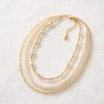 Cassia convertible pearl layered necklace featuring Swarovski® Crystal Pearls, gold tube strand and paperclip chain displayed on white quartz.