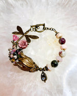 Close-up of the Dragonfly Garden Reverie Bracelet showing the Vintaj brass dragonfly, pink glass blossoms, and mixed tourmaline gemstones, handcrafted by Carabella by Cheryl.