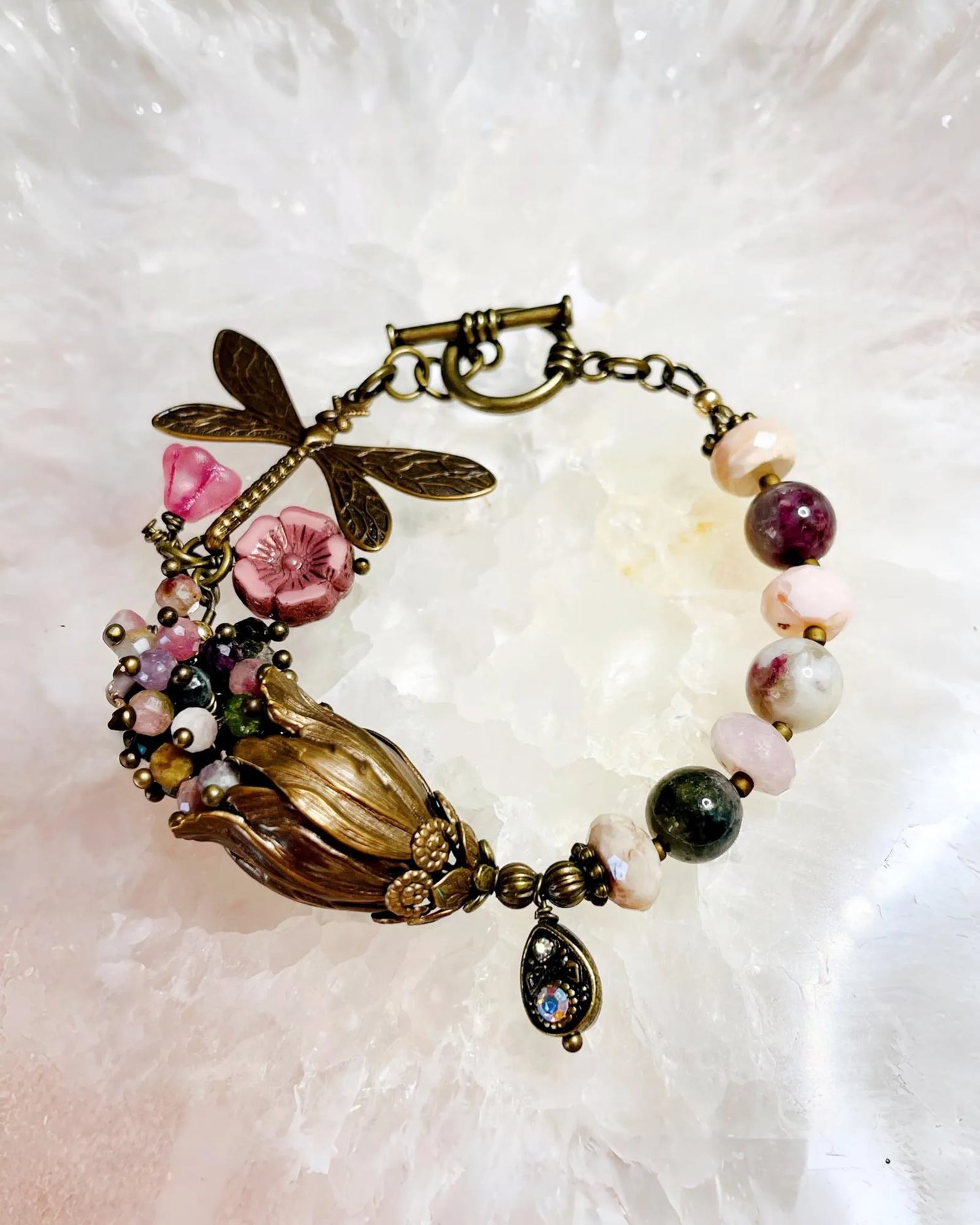 Close-up of the Dragonfly Garden Reverie Bracelet showing the Vintaj brass dragonfly, pink glass blossoms, and mixed tourmaline gemstones, handcrafted by Carabella by Cheryl.