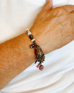 Model wearing the Dragonfly Garden Reverie Bracelet by Carabella by Cheryl, featuring Vintaj brass, tourmaline gemstones, and floral charms in an elegant botanical design.