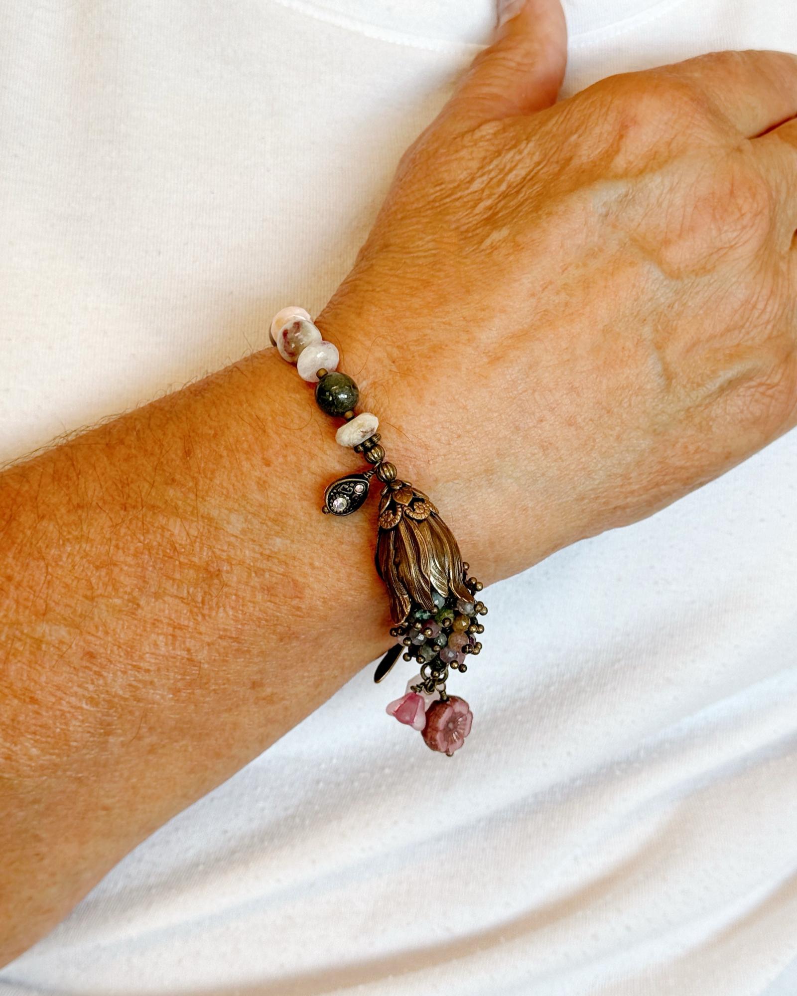 Model wearing the Dragonfly Garden Reverie Bracelet by Carabella by Cheryl, featuring Vintaj brass, tourmaline gemstones, and floral charms in an elegant botanical design.