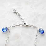 Rear clasp detail of the Ella silver charm bracelet featuring the polished lobster clasp, adjustable extender chain, signature tag, and sapphire blue crystal drops handcrafted in sterling silver.
