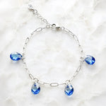 Ella silver charm bracelet with four sapphire blue crystal pear drops displayed on white quartz.