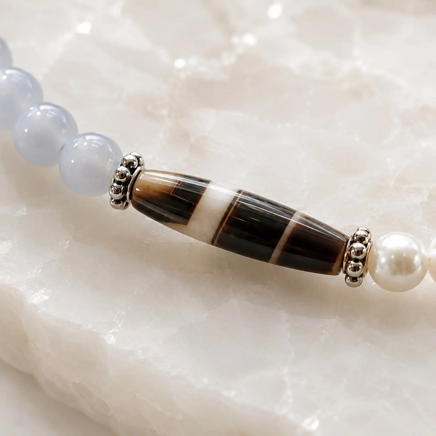 Macro detail of the Elodie Bracelet showcasing the Tibetan agate focal stone, blue chalcedony gemstones, Snow Czech crystal pearls, and sterling silver spacer rings.