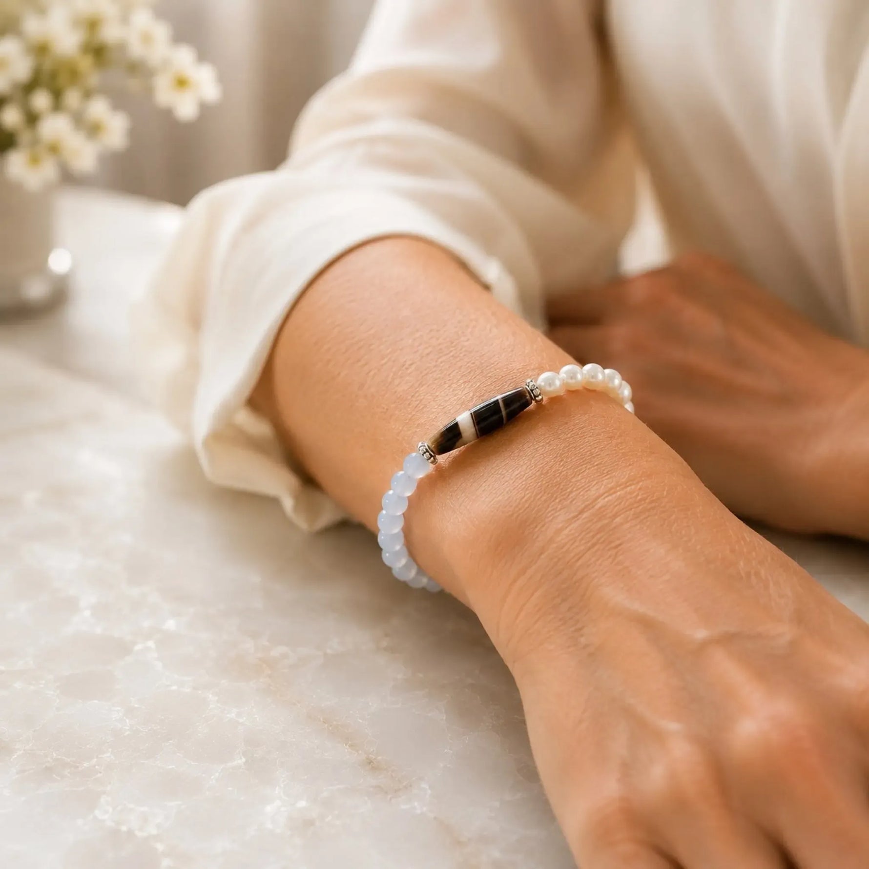 Close-up of the Elodie Blue Chalcedony & Snow Czech Crystal Pearl Bracelet worn on the wrist with an ivory blouse in soft natural light.