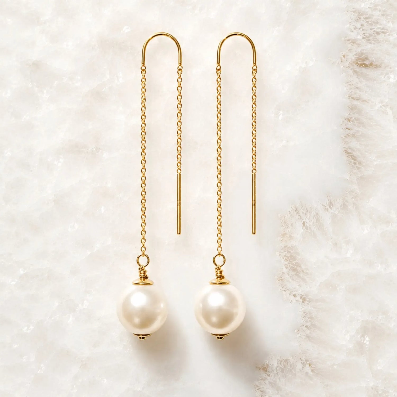 Handcrafted gold threader pearl earrings with Swarovski® Crystal Pearls displayed on white quartz.
