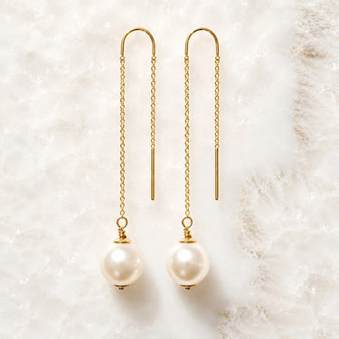 Handcrafted gold threader pearl earrings with Swarovski® Crystal Pearls displayed on white quartz.