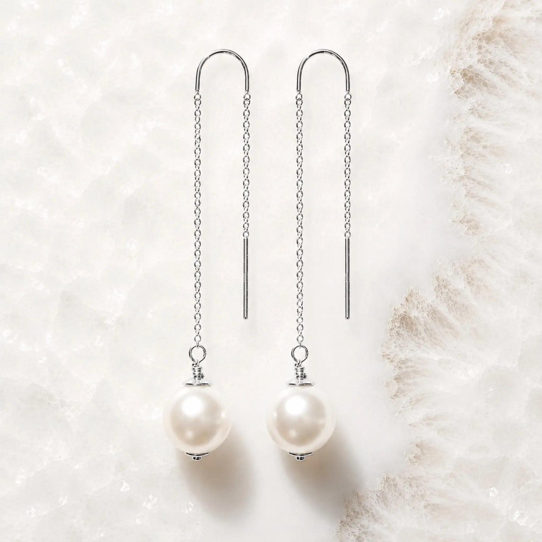 Handcrafted sterling silver threader pearl earrings with Swarovski® Crystal Pearls displayed on white quartz.
