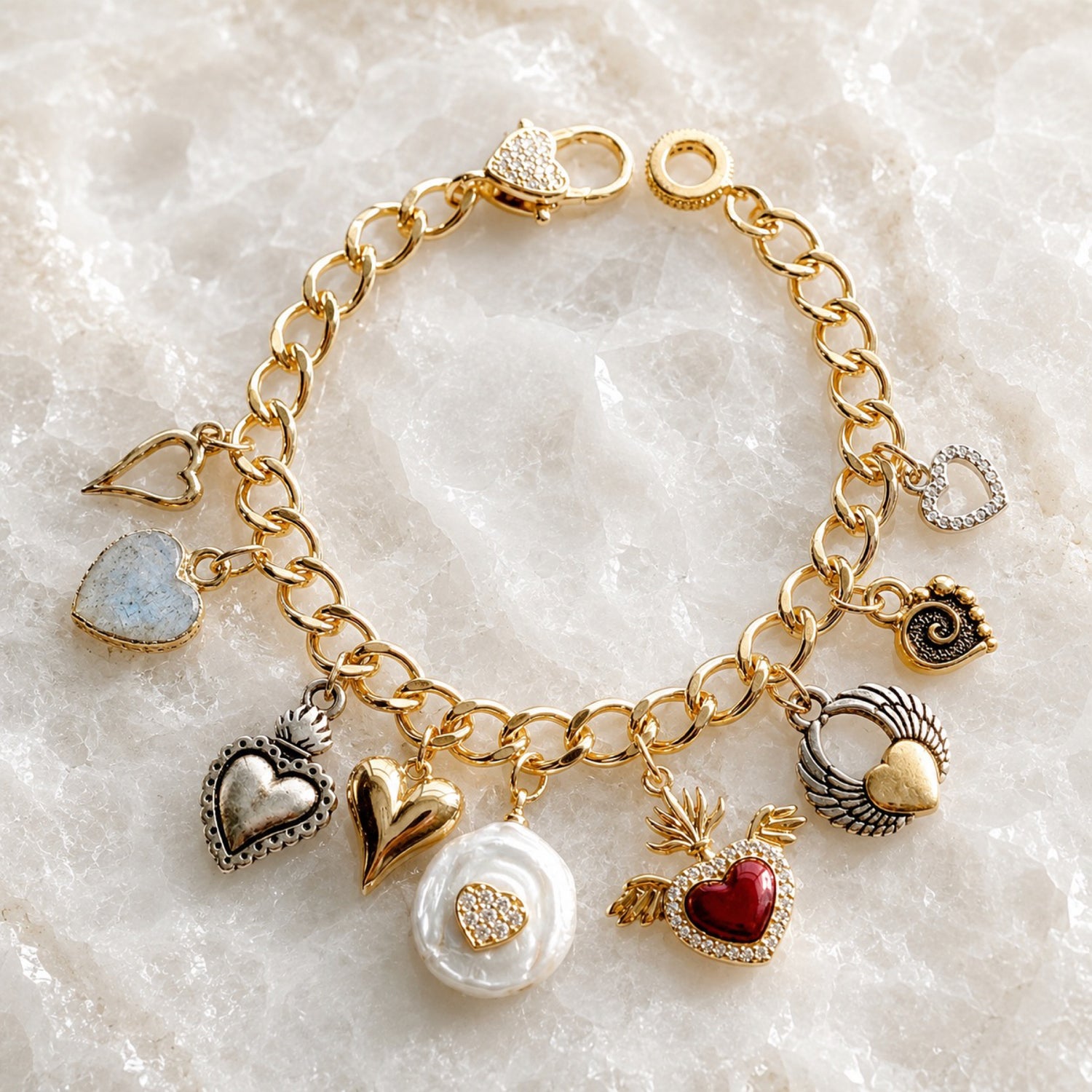 Esme Gold Charm Bracelet on white quartz featuring handcrafted heart charms, crystal heart clasp, pearl charm, enamel heart, and mixed-metal accents by Carabella by Cheryl.
