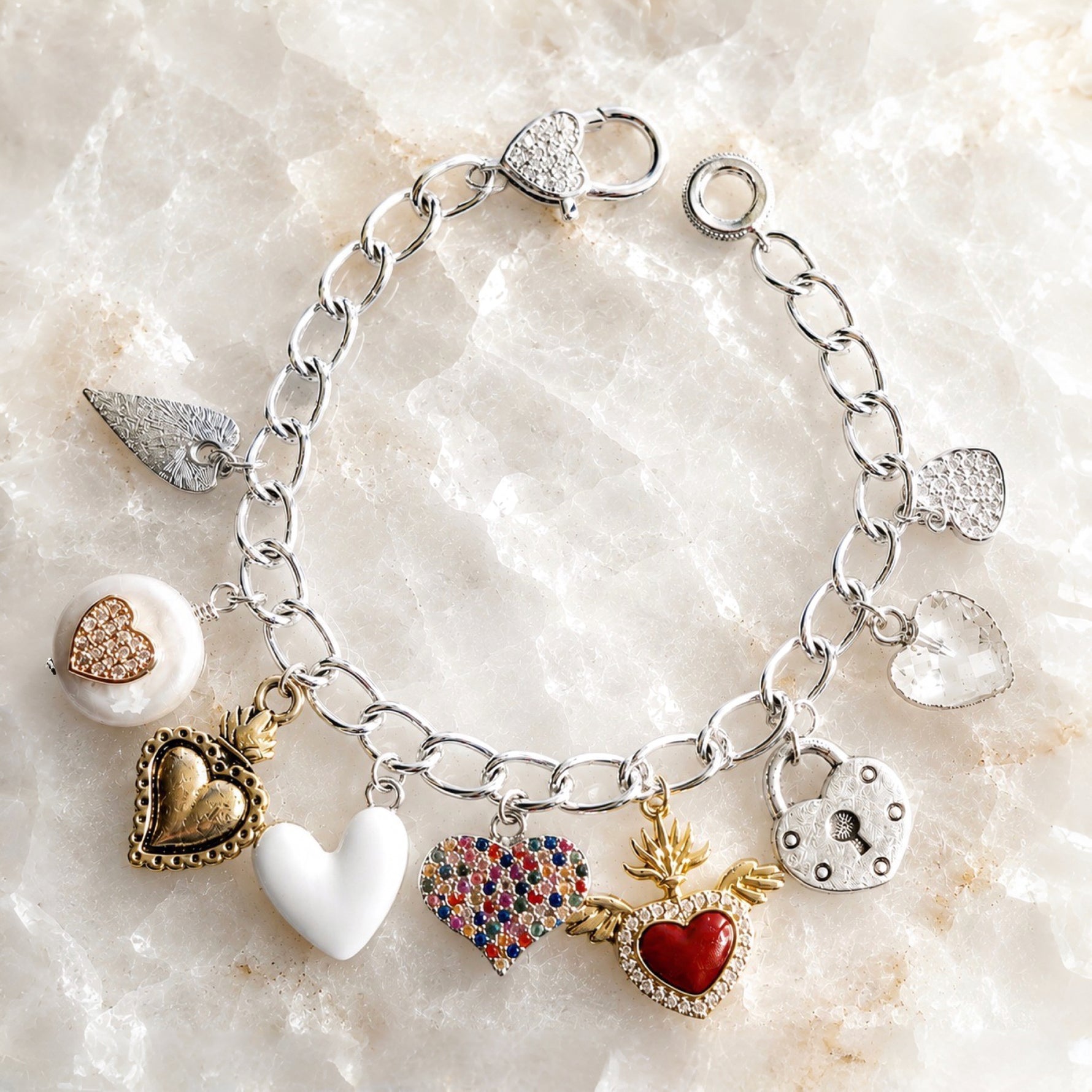 Esme Silver Charm Bracelet on white quartz featuring heart charms, crystal heart clasp, pearl charm, enamel heart, and handcrafted mixed-metal design by Carabella by Cheryl.