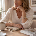 Woman wearing the Esme Silver Charm Bracelet with an ivory cashmere sweater in a refined everyday lifestyle setting.