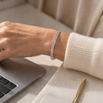 Woman wearing the Evelyn fine silver bracelet with an ivory cashmere sweater while working at a desk, illustrating refined everyday luxury.
