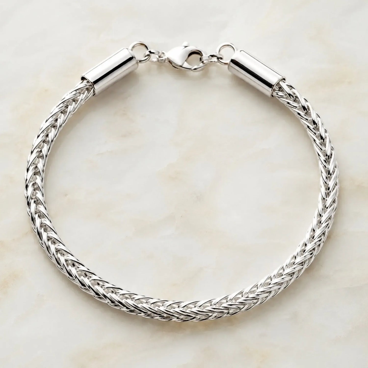 Evelyn fine silver handwoven bracelet displayed in a perfect circular shape on a soft quartz surface, showcasing the intricate woven silver design and polished lobster clasp.
