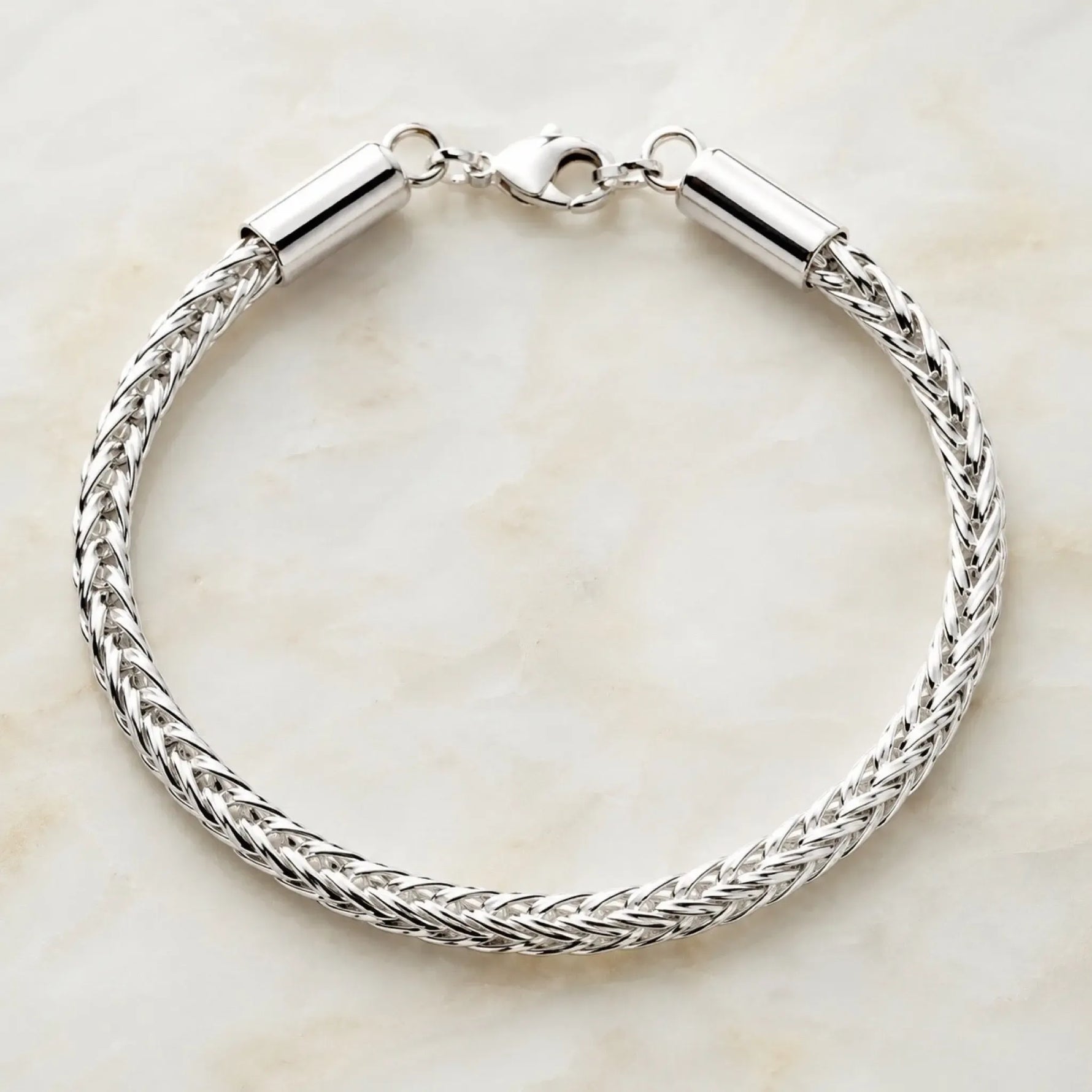 Evelyn fine silver handwoven bracelet displayed in a perfect circular shape on a soft quartz surface, showcasing the intricate woven silver design and polished lobster clasp.