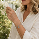 Woman wearing the Flora handwoven .999 fine silver bracelet while admiring blooming flowers in a botanical garden, highlighting its floral-inspired design.