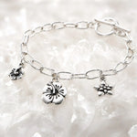 Angled editorial photograph of the Flora handwoven .999 fine silver bracelet with floral charms on luminous white quartz.