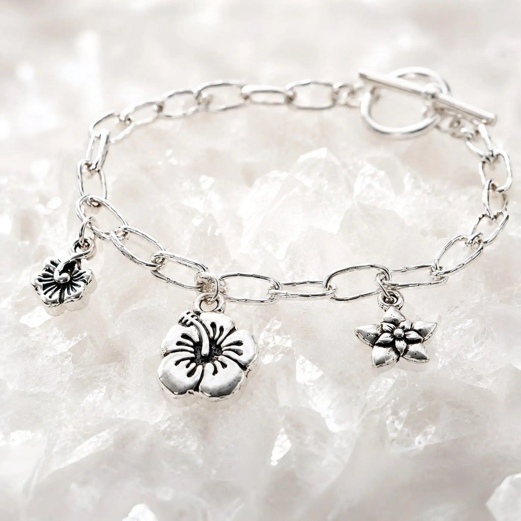 Angled editorial photograph of the Flora handwoven .999 fine silver bracelet with floral charms on luminous white quartz.