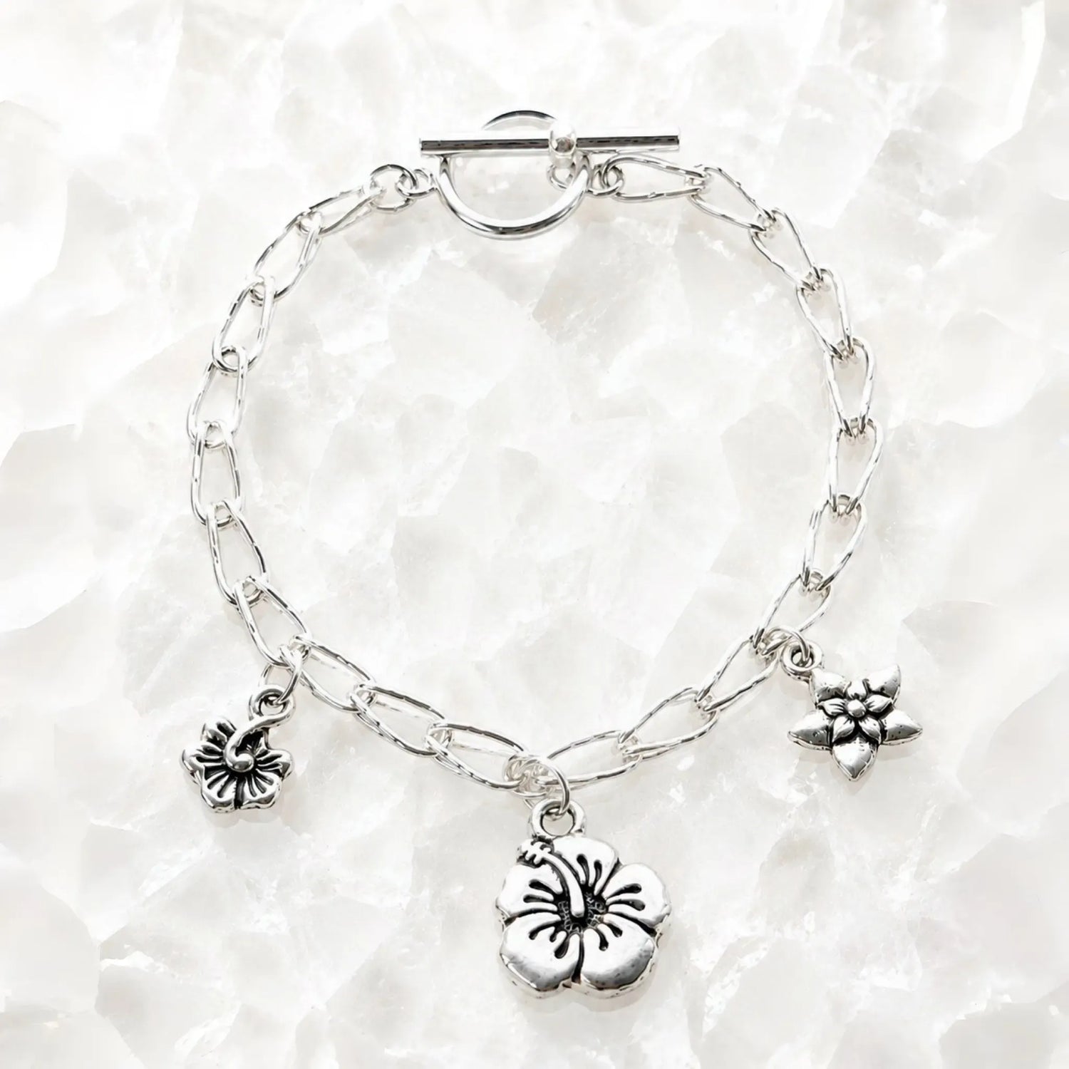 Flora handwoven .999 fine silver bracelet with three floral pewter charms displayed on luminous white quartz, handcrafted in Canada.