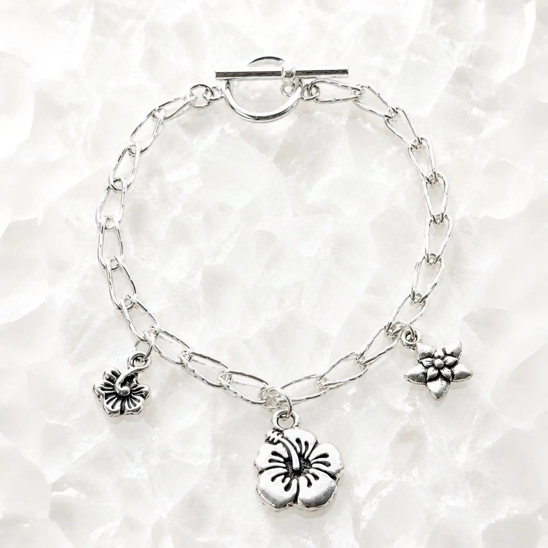 Flora handwoven .999 fine silver bracelet with three floral pewter charms displayed on luminous white quartz, handcrafted in Canada.