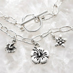 Close-up of the Flora bracelet highlighting the handwoven .999 fine silver links, sterling silver toggle clasp and floral pewter charms on white quartz.
