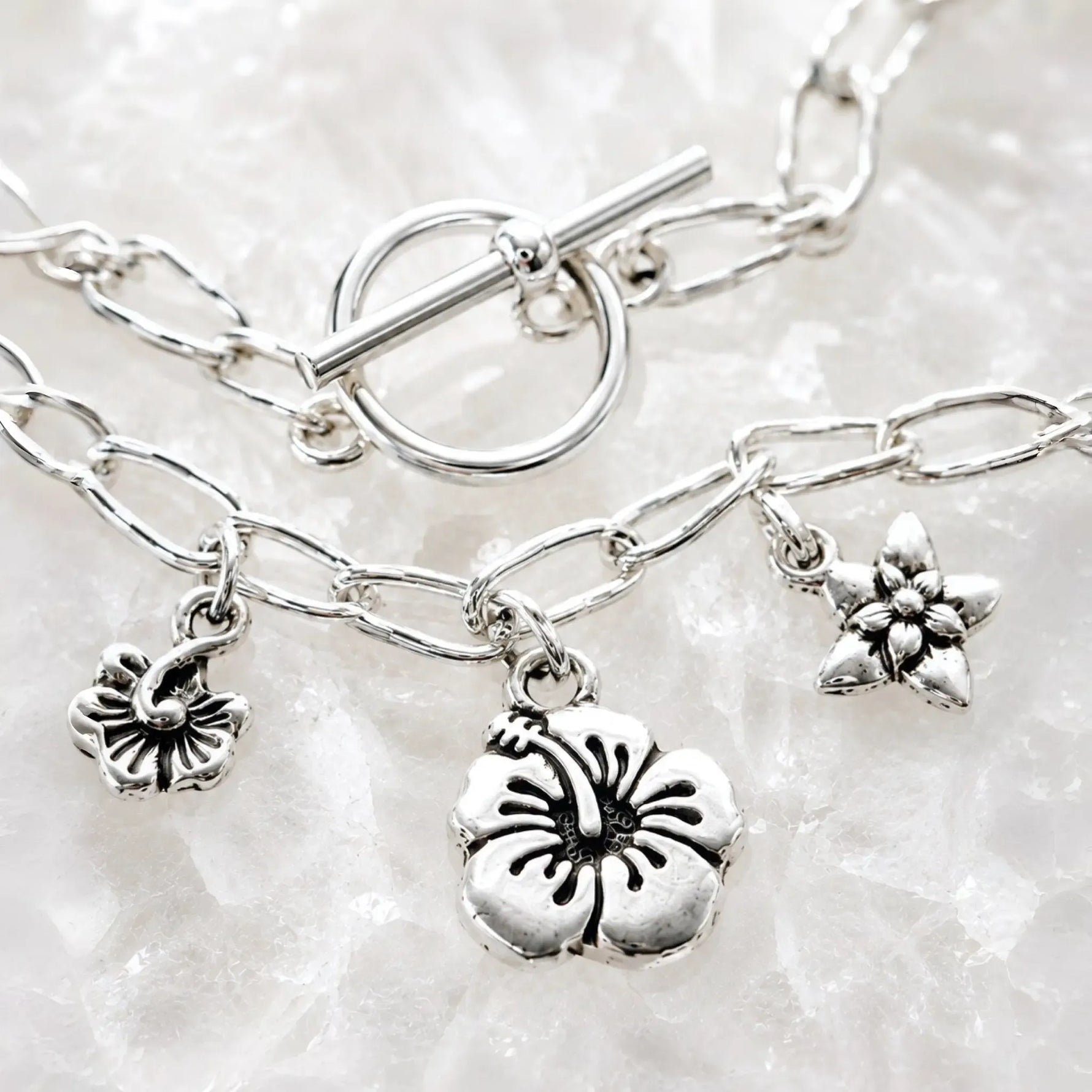 Close-up of the Flora bracelet highlighting the handwoven .999 fine silver links, sterling silver toggle clasp and floral pewter charms on white quartz.