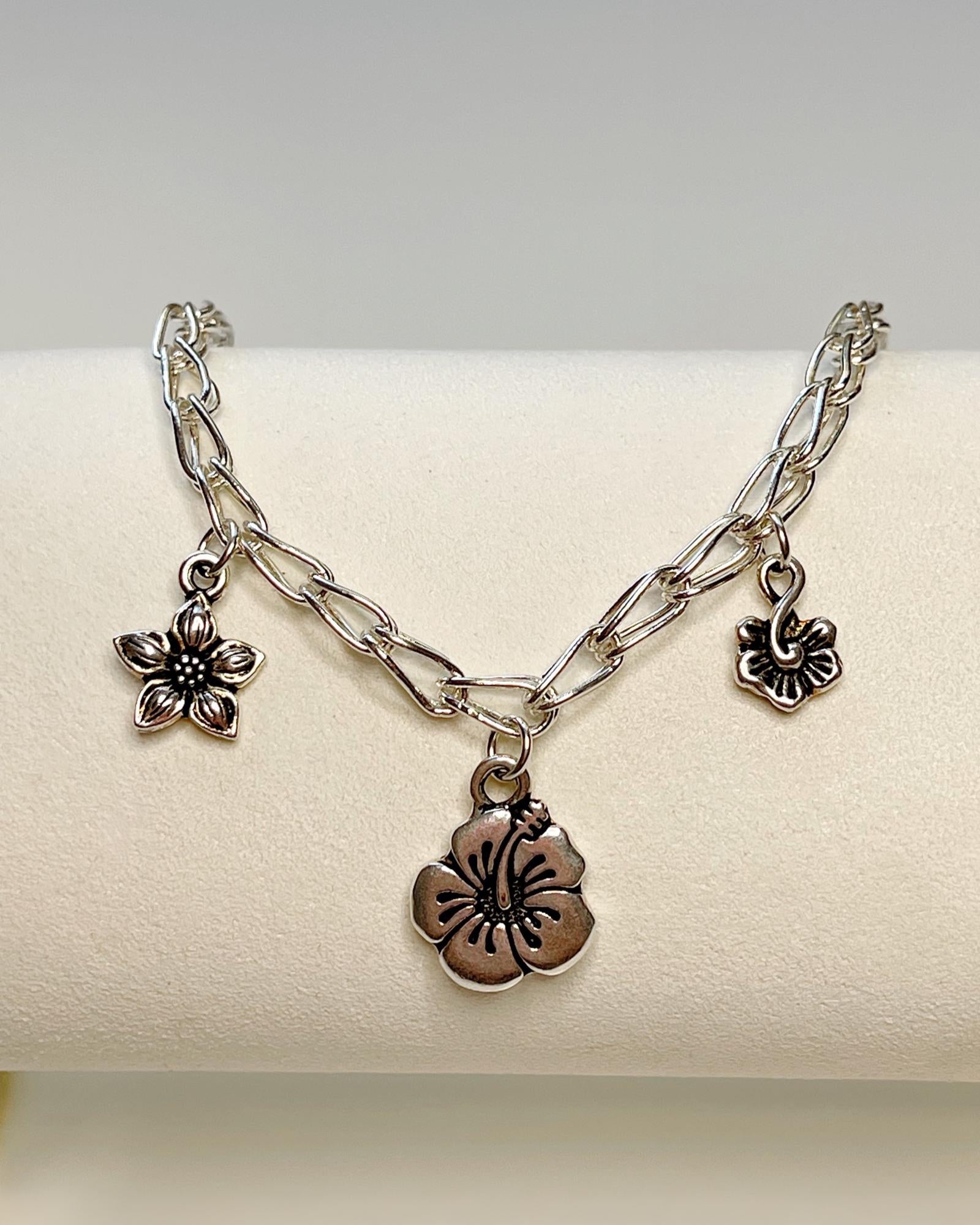 Flora bracelet displayed on a white jewelry stand, featuring a sterling silver chain and botanical flower charms, handcrafted in Canada by Carabella by Cheryl.