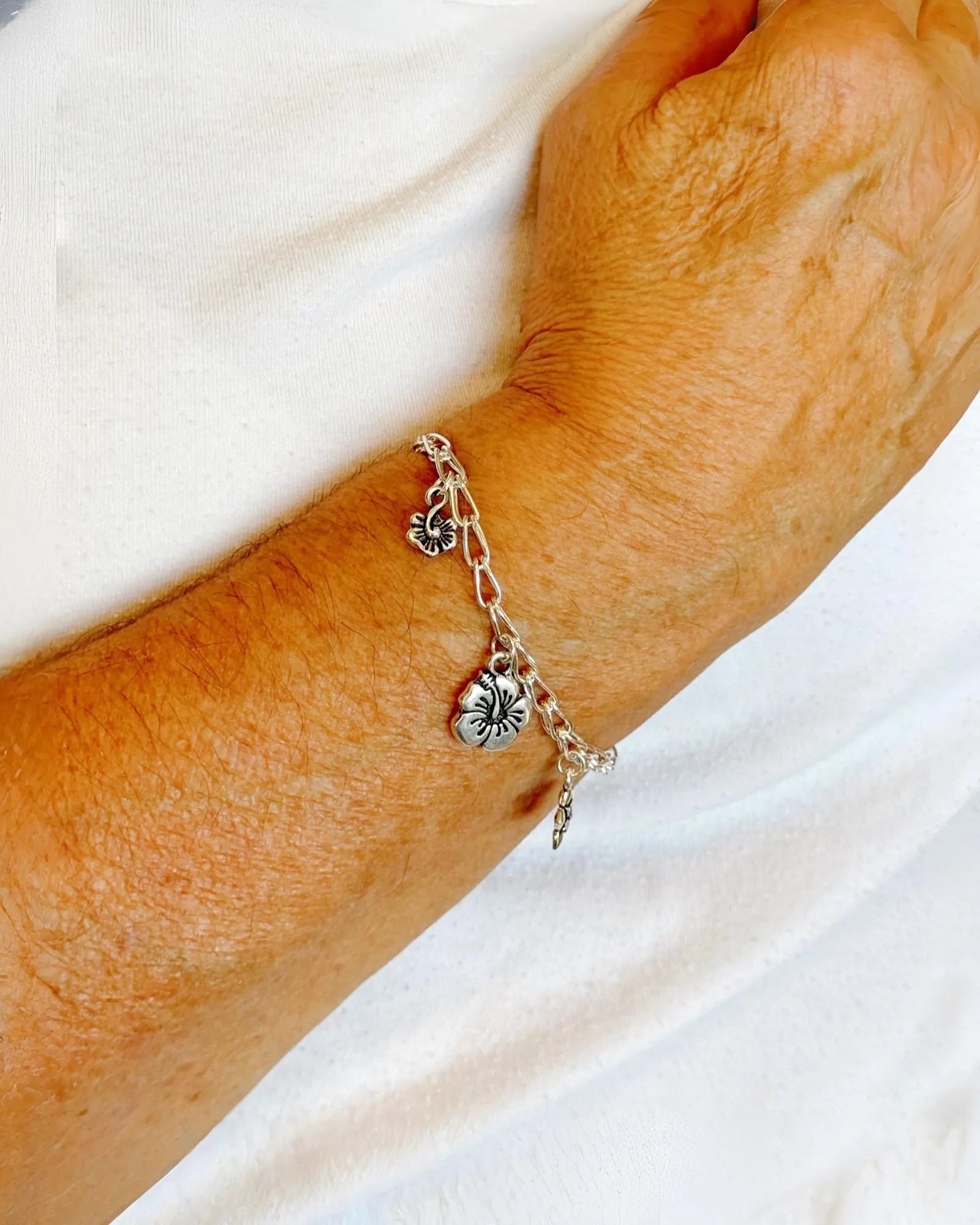 Model wearing the Flora sterling silver charm bracelet with delicate botanical flower charms, handcrafted by Carabella by Cheryl.
