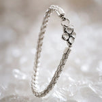 Gemma handwoven .999 fine silver bracelet standing in a graceful curve on white quartz, highlighting the dimensional woven silver construction and sterling silver apple blossom clasp.