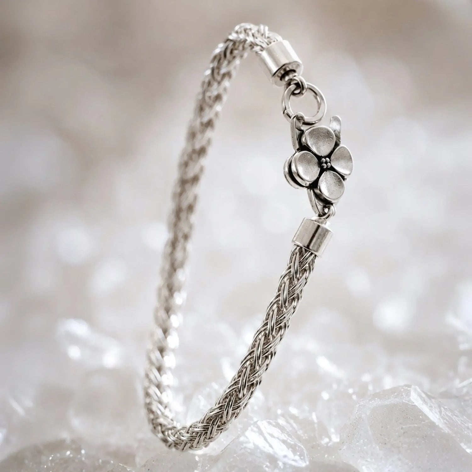 Gemma handwoven .999 fine silver bracelet standing in a graceful curve on white quartz, highlighting the dimensional woven silver construction and sterling silver apple blossom clasp.