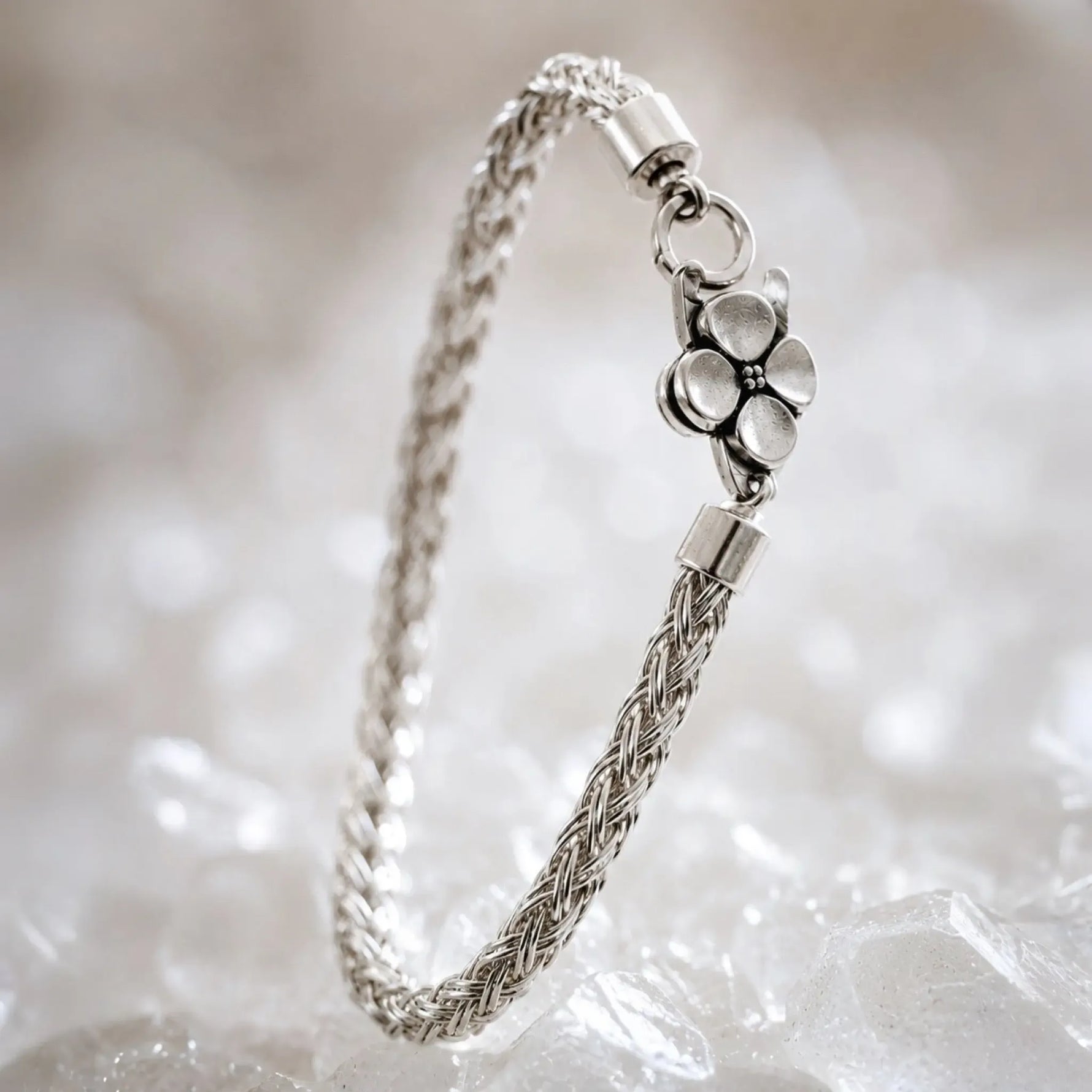 Gemma handwoven .999 fine silver bracelet standing in a graceful curve on white quartz, highlighting the dimensional woven silver construction and sterling silver apple blossom clasp.